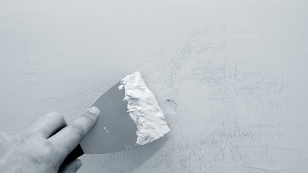 a person using a paint scraper for hole patching